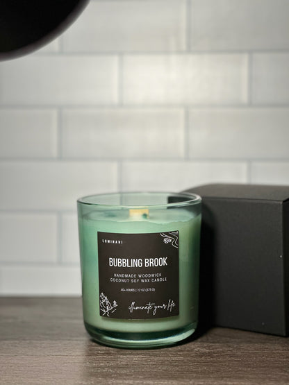 Green candle labeled 'Bubbling Brook' on a wooden surface with a white tiled wall background